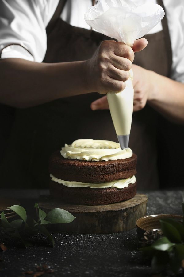Dana finishing a wedding tier &mdash; piping cream onto a two-tier chocolate cake.