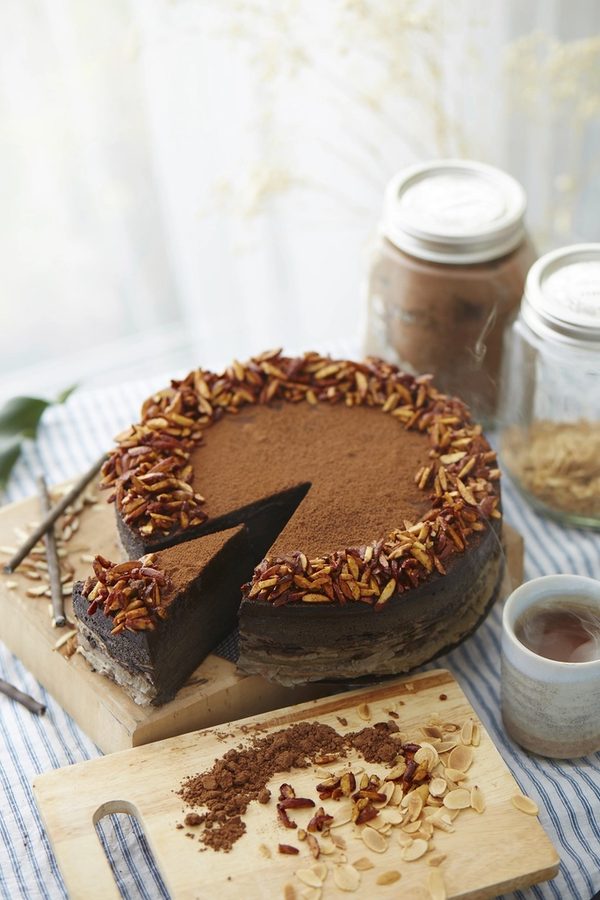 The chocolate espresso cake with a slice cut, on a wooden board by the window.