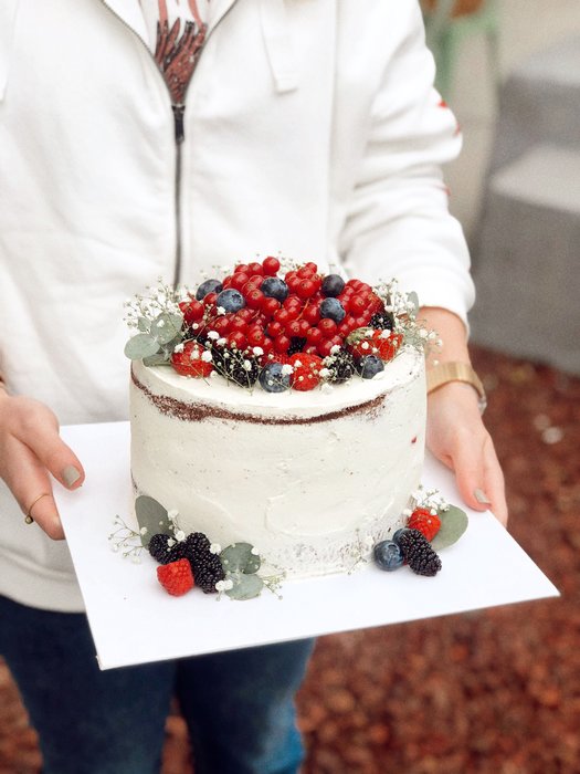 A small berry-topped layer cake held out in two hands, ready to be handed over.