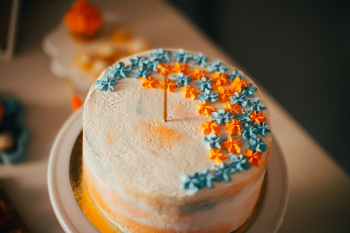 A tall birthday cake covered in tiny blue and orange piped flowers, a single candle on top.