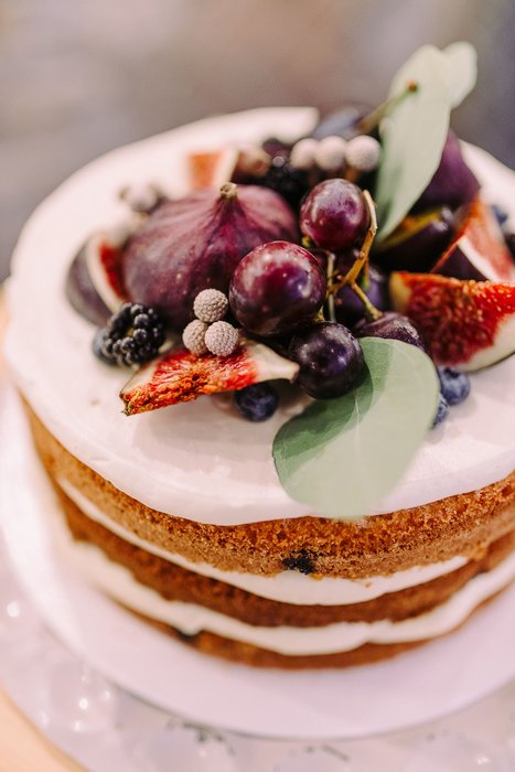 A naked layer cake topped with figs, grapes and eucalyptus leaves.