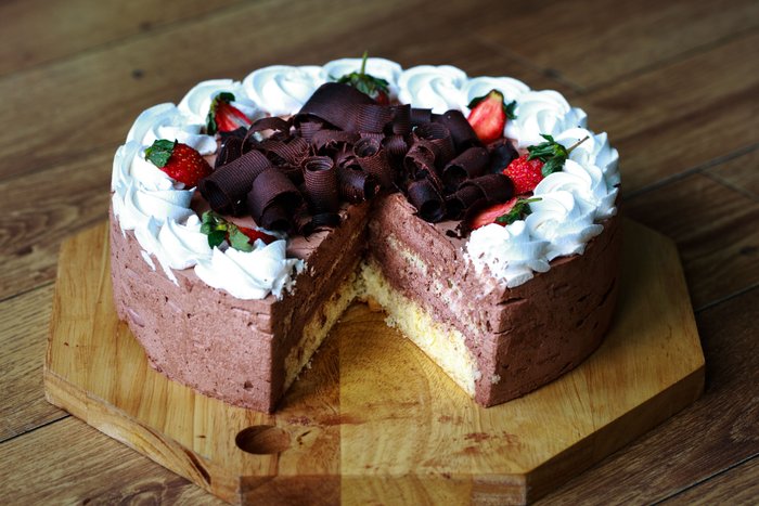A chocolate cake with whipped cream and strawberries, one slice cut away.
