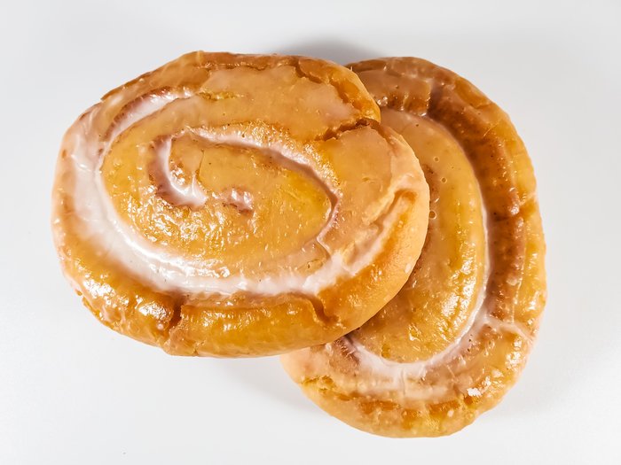 Two iced cinnamon rolls on a white counter, seen from above.