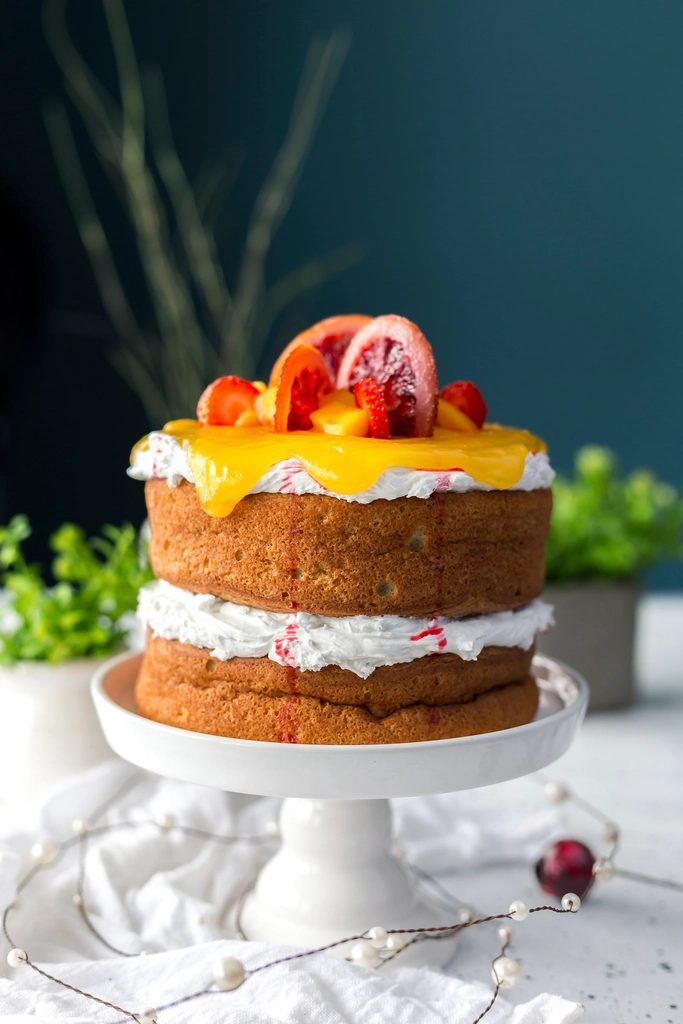 The naked lemon-berry layer cake on a white cake stand, topped with citrus slices and berries.