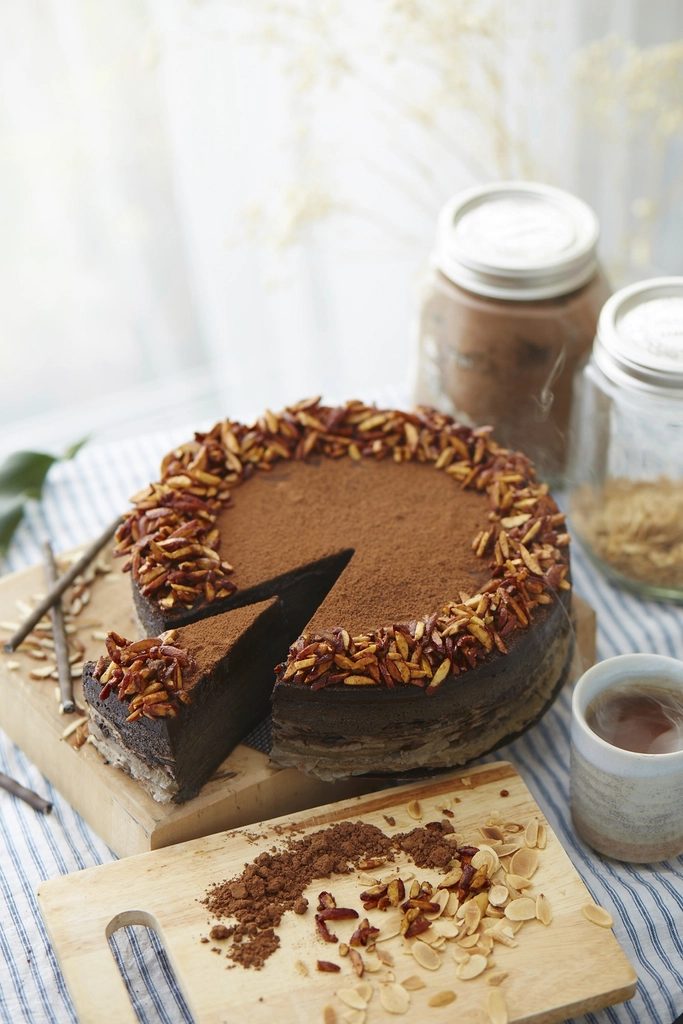The chocolate espresso cake with a slice cut, on a wooden board by the window.