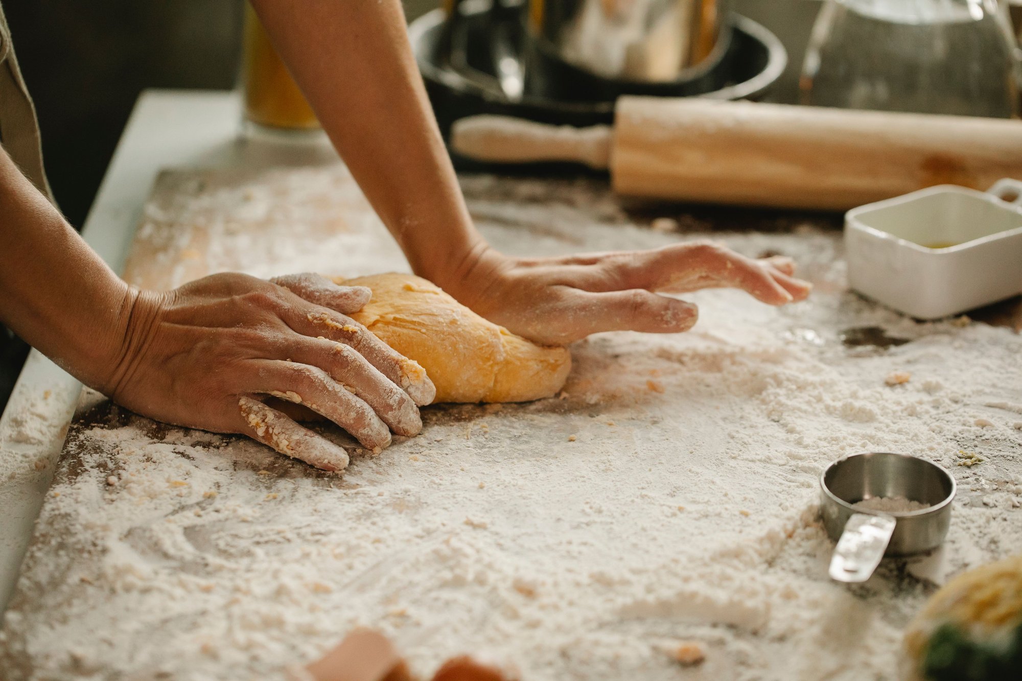 A baker&rsquo;s hands pressing dough into a floured wooden bench, seen from above.