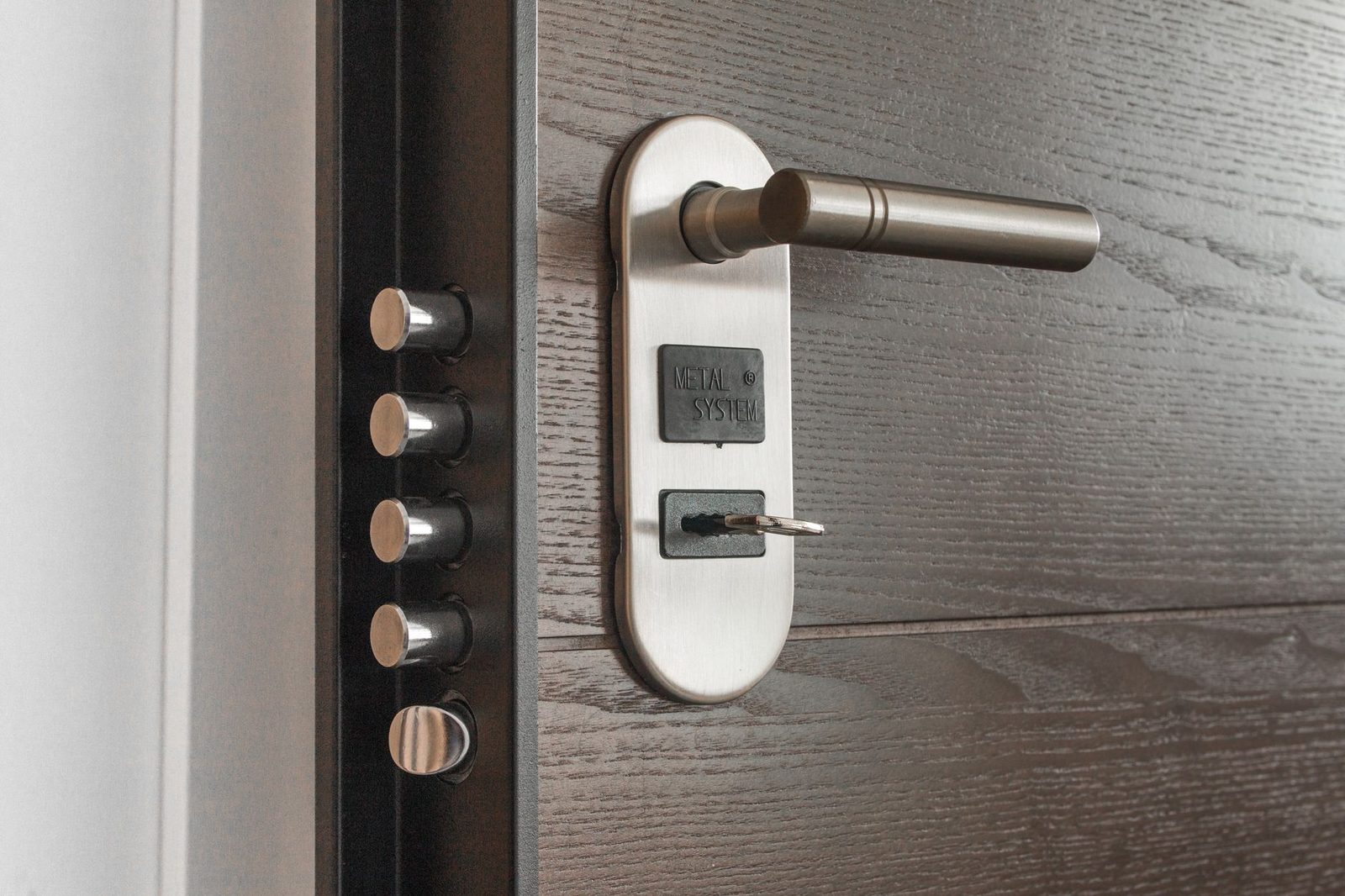 A brushed-steel lever handle on a dark grey door with a key left in the cylinder and the deadbolt pins along the jamb.