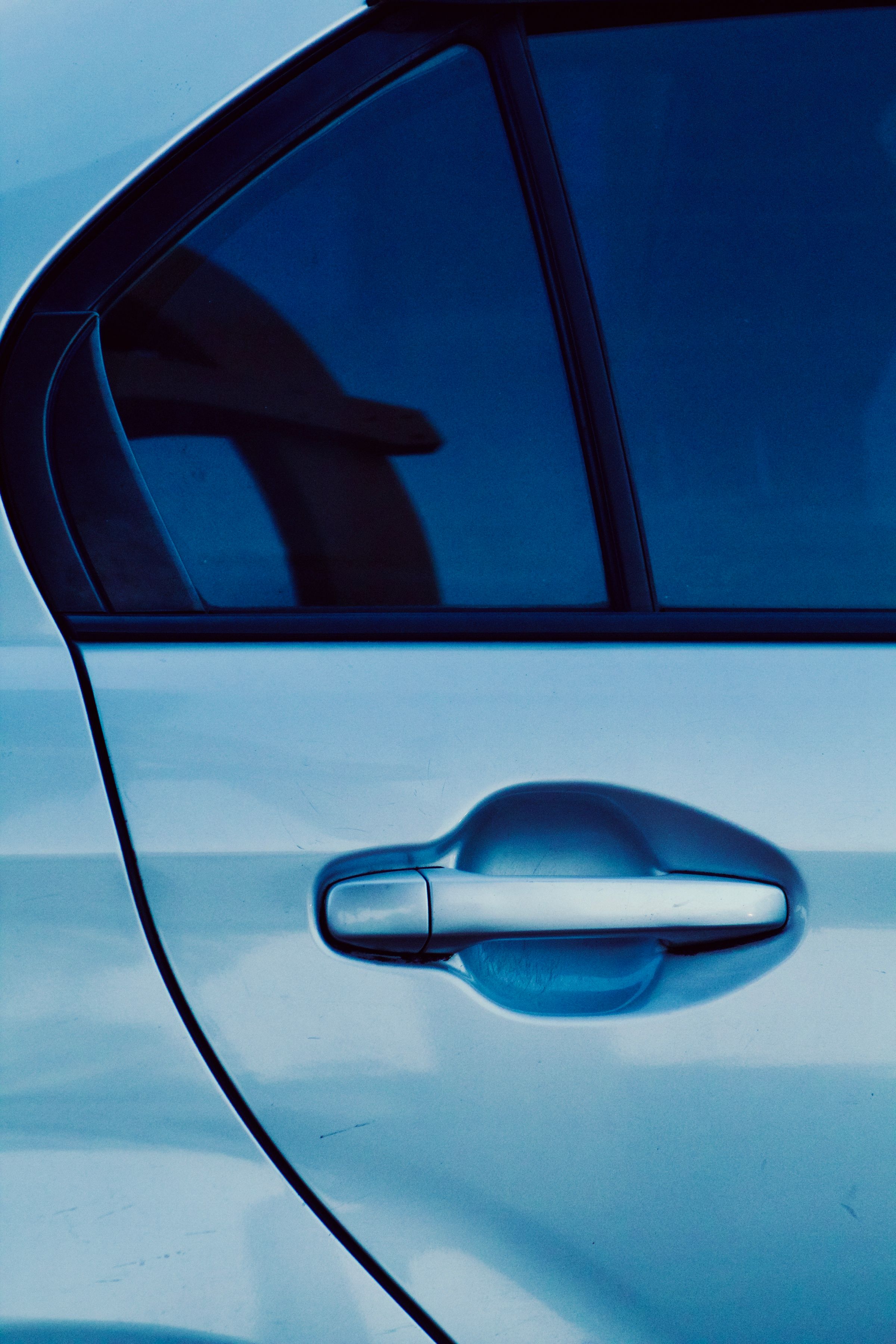 The rear door and chrome handle of a silver sedan under cold blue light.