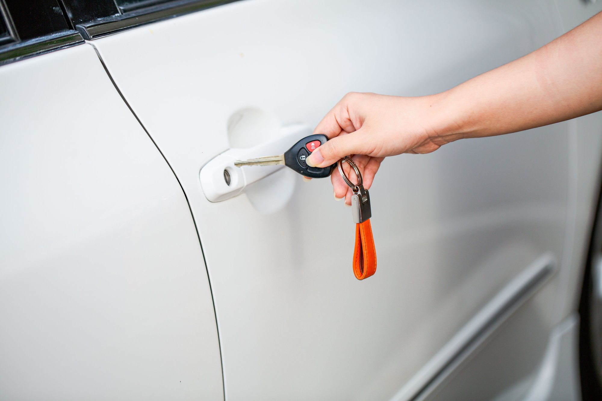 A hand fitting a key into the driver’s door of a white car.