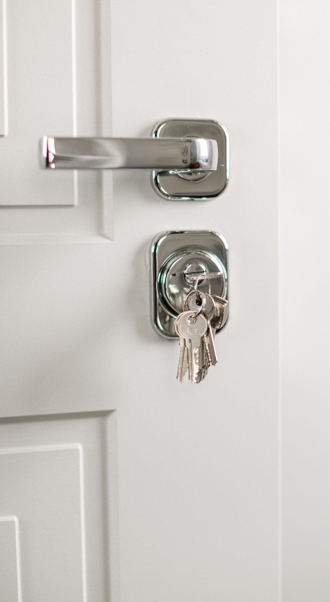 A modern silver lever handle on a white door, keys hanging from the lock beneath it.