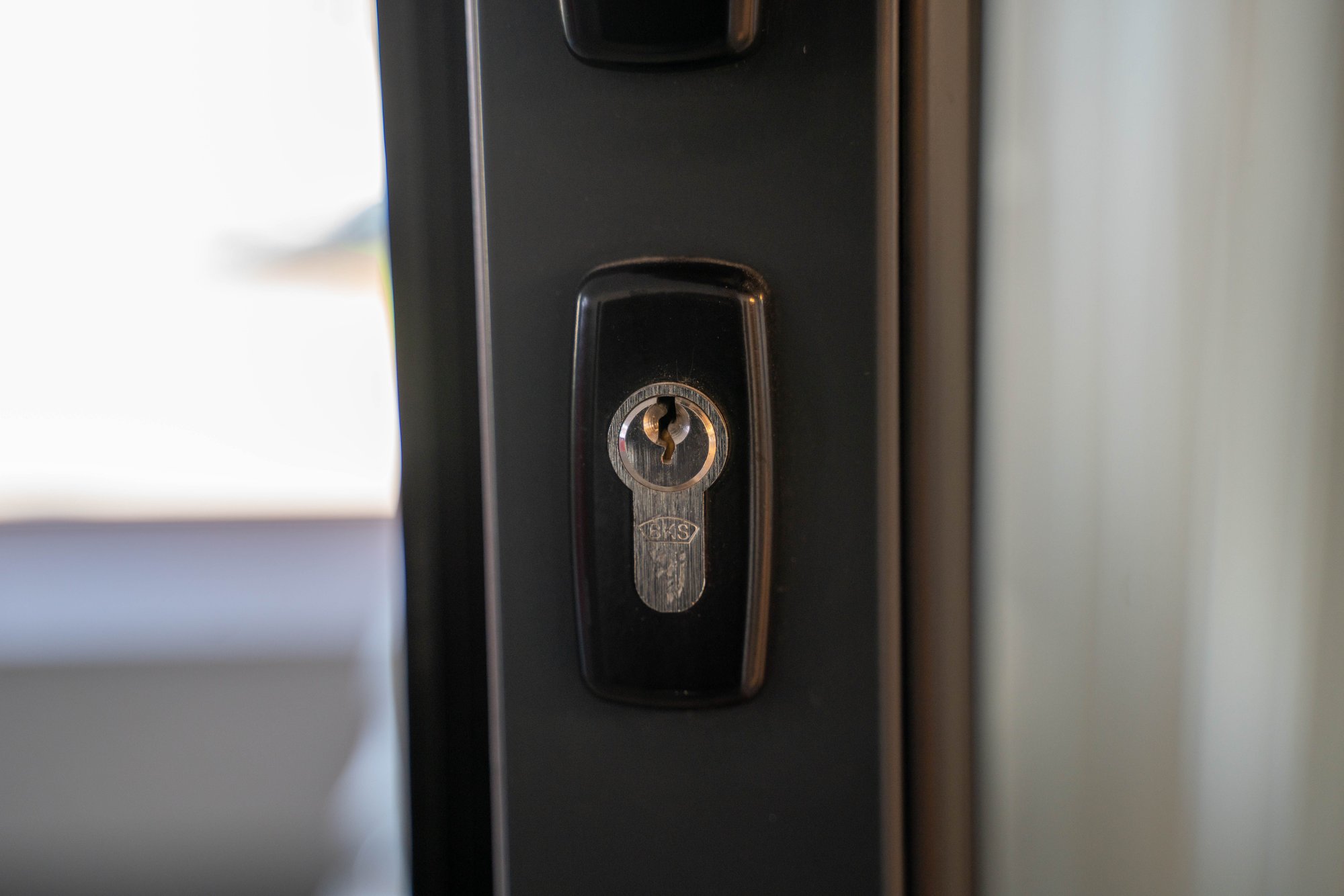 A brushed-steel keyhole plate set into the edge of a dark grey door.