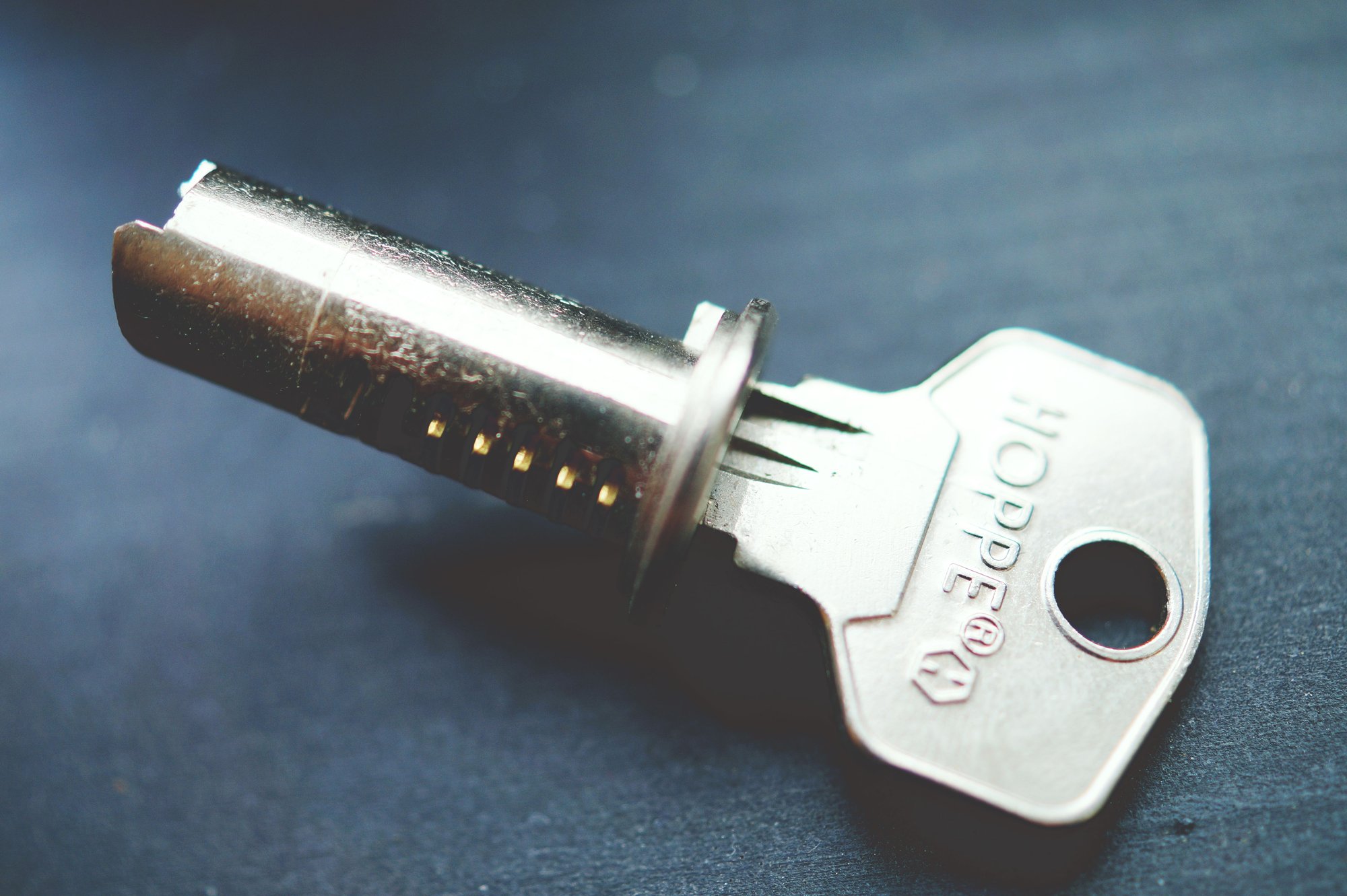 A lock cylinder pulled from its housing, lying next to its key on a dark bench.