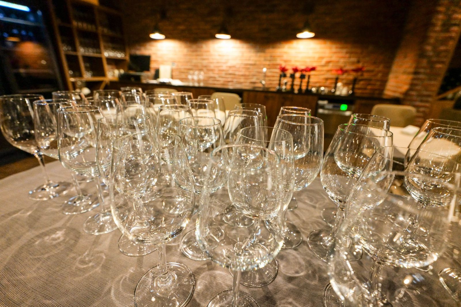 Rows of empty wine and champagne glasses on a linen-covered table in front of a warm brick wall