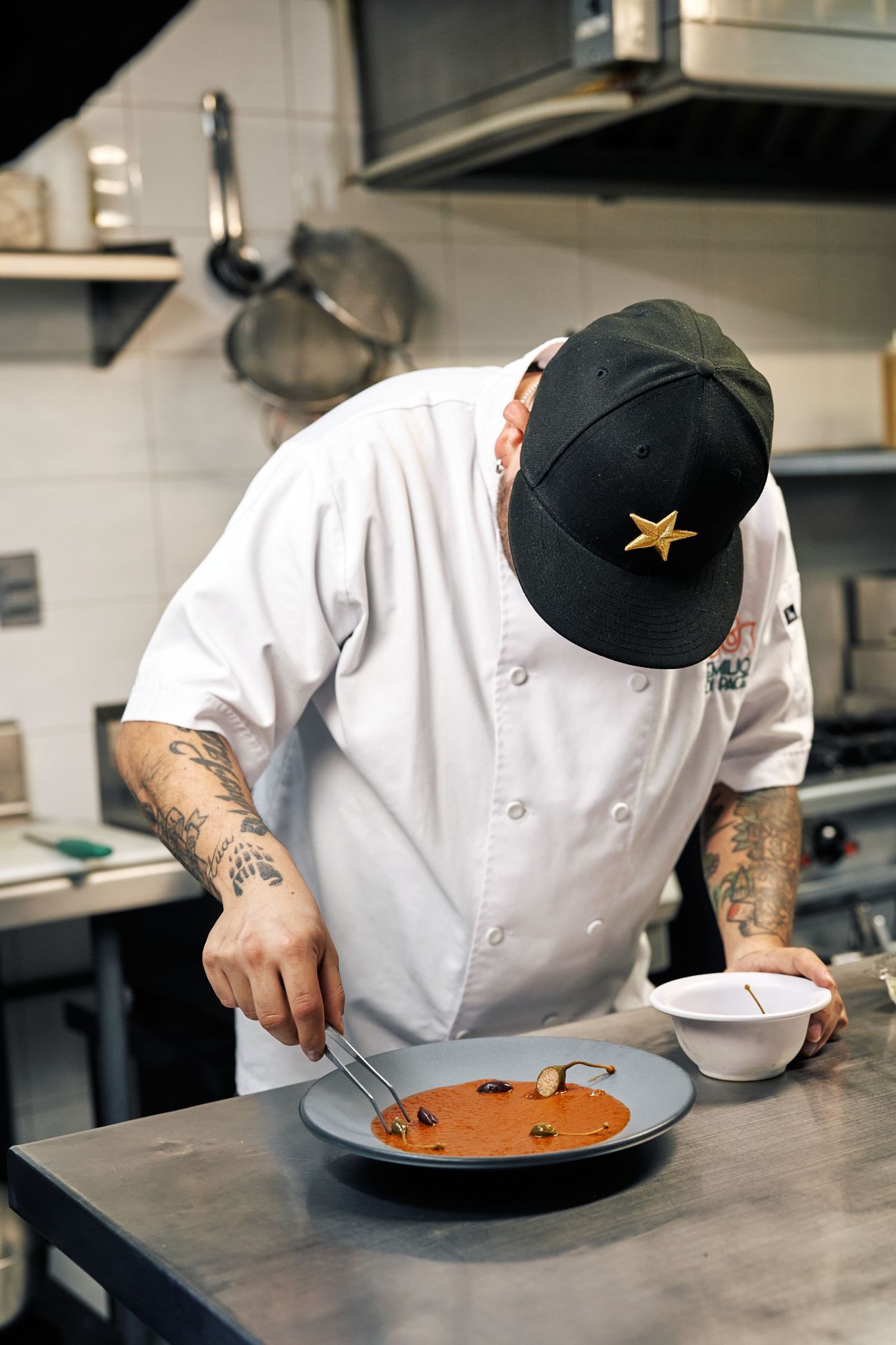 A cook in whites bent over the bench, finishing a plate of soup by hand
