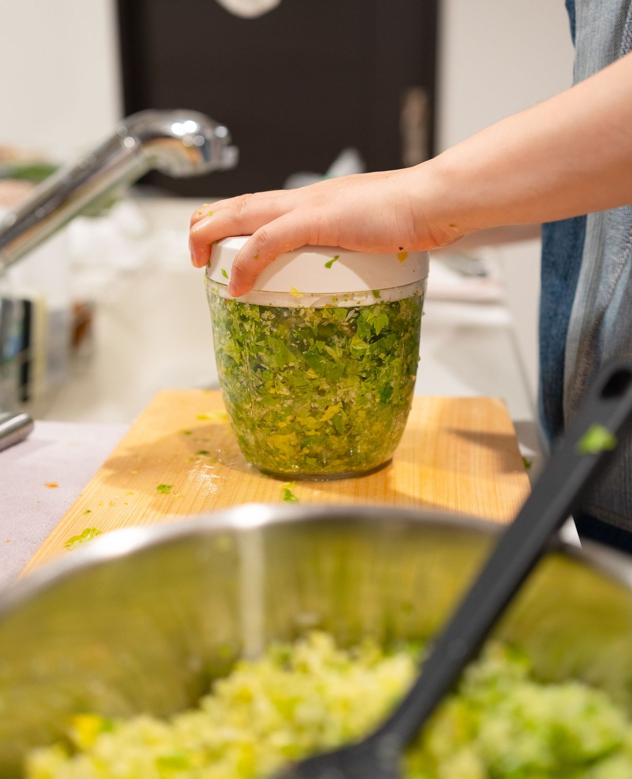 Hands working a hand chopper through herbs over a bowl on a wooden board