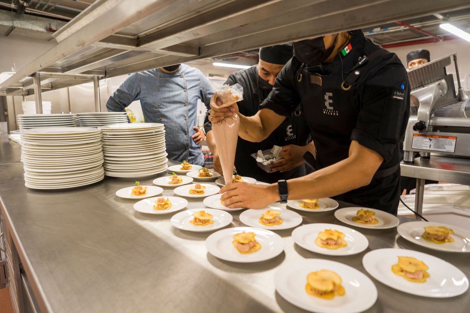 Cooks working down a long pass, plating rows of identical dishes for service