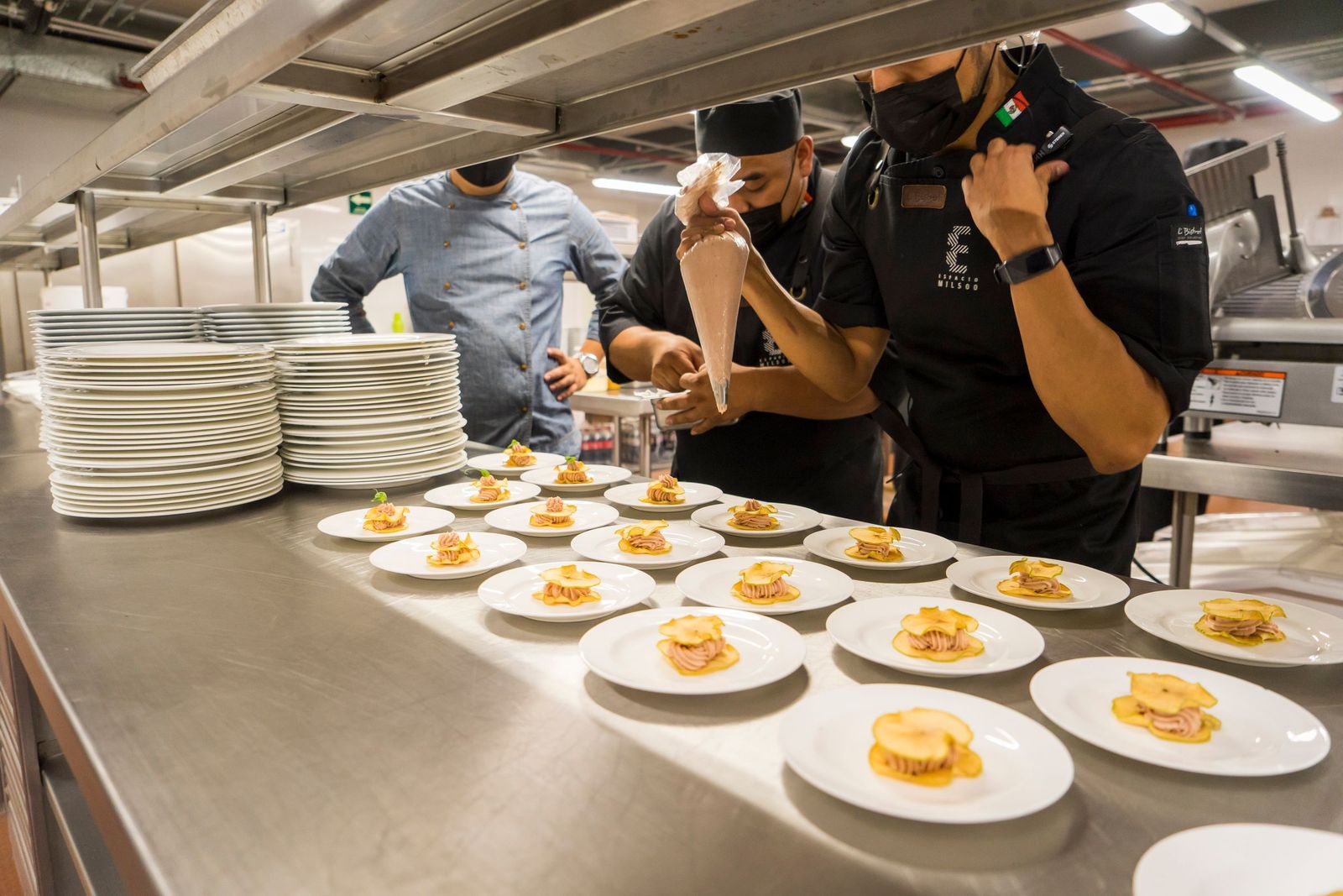 A team working side by side down the pass, plating appetisers together