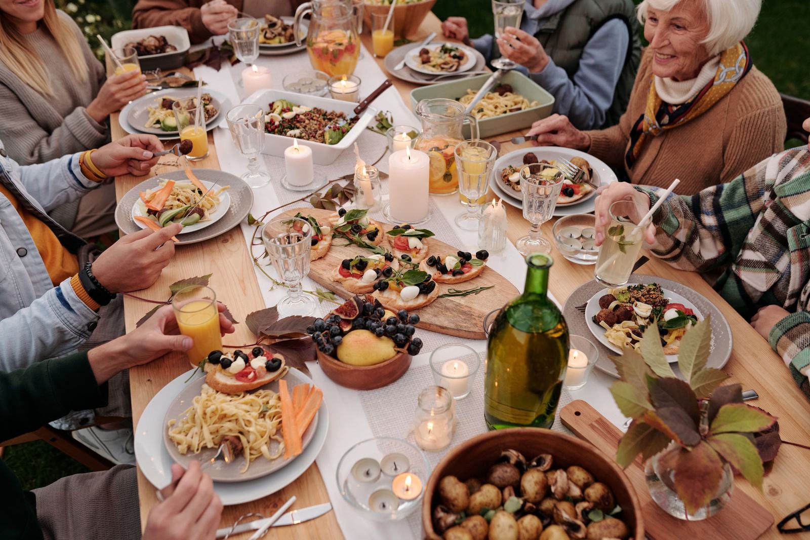 Seen from above, a table mid-meal: shared plates, glasses and hands reaching across