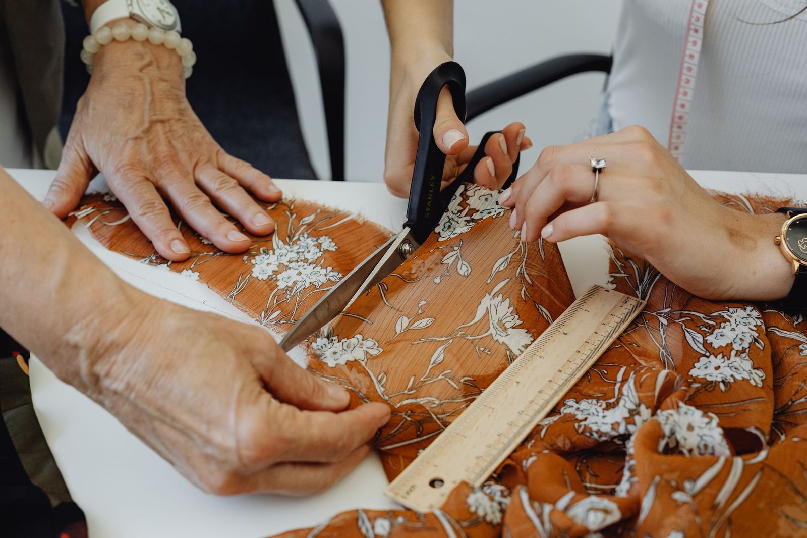 Two people at a workbench cutting patterned fabric with shears, a ruler and a tape measure beside them