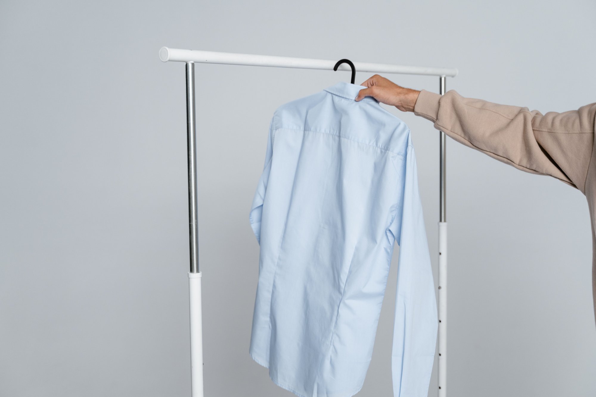 A hand hanging a pressed light-blue shirt on a white rail.