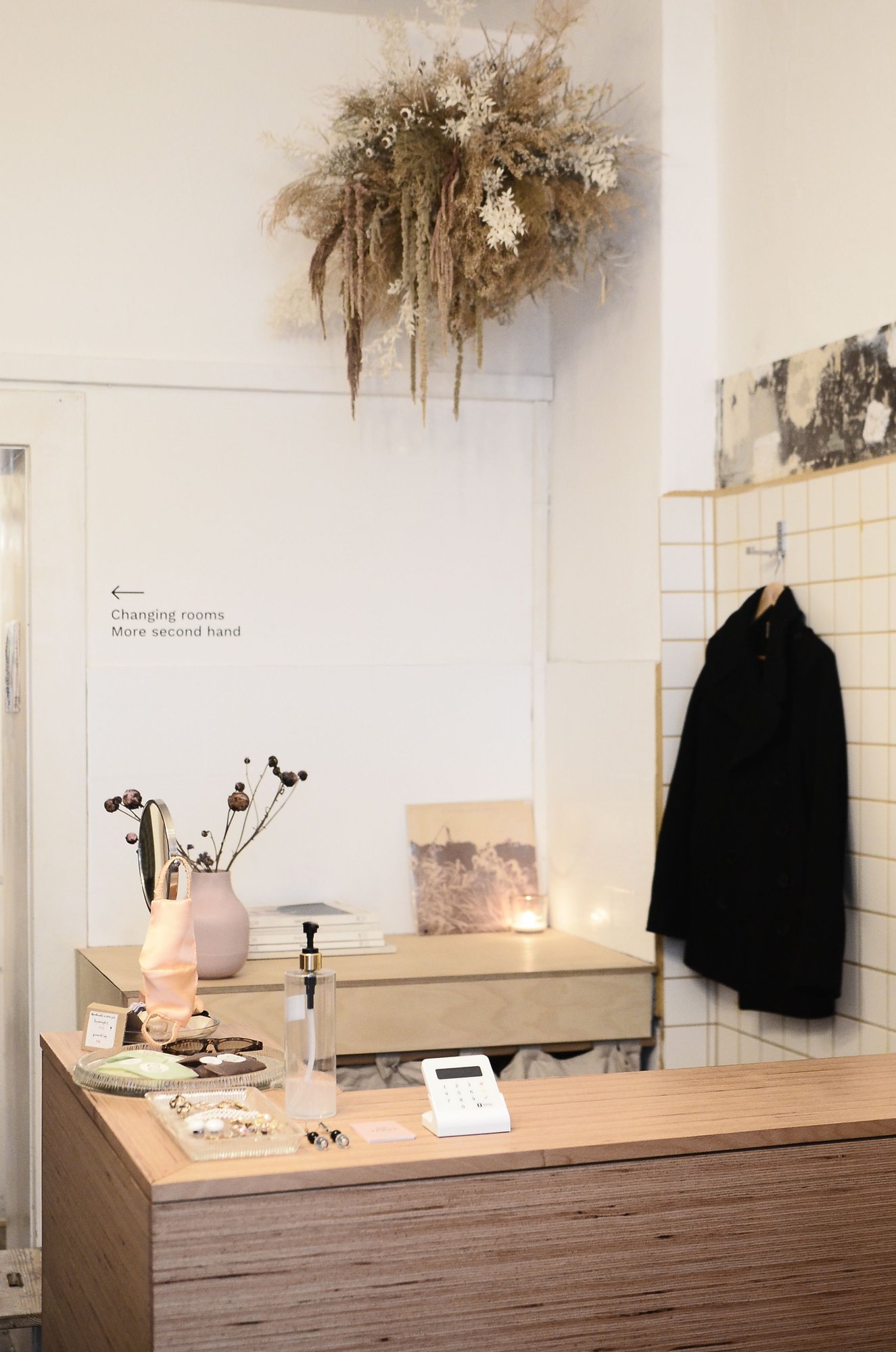 A calm, light-filled shop interior with a dark coat on a hanger beside a small desk.