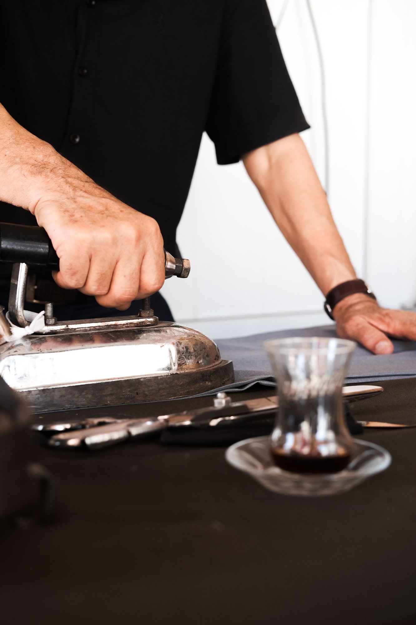 Hands working a vintage iron across cloth on a pressing table.