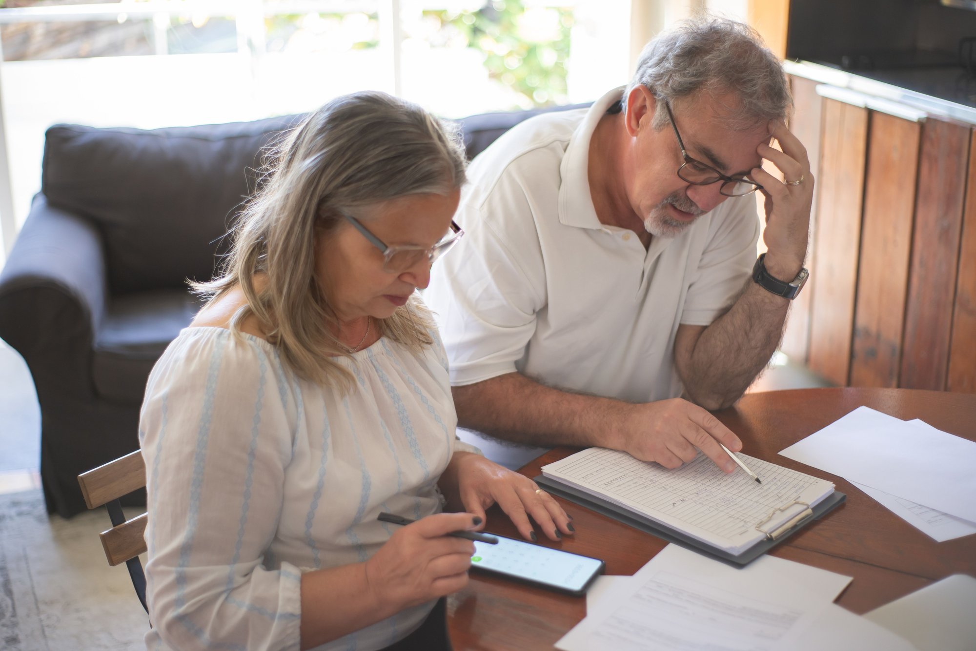 An older couple on a sofa reading a document together, glasses on.
