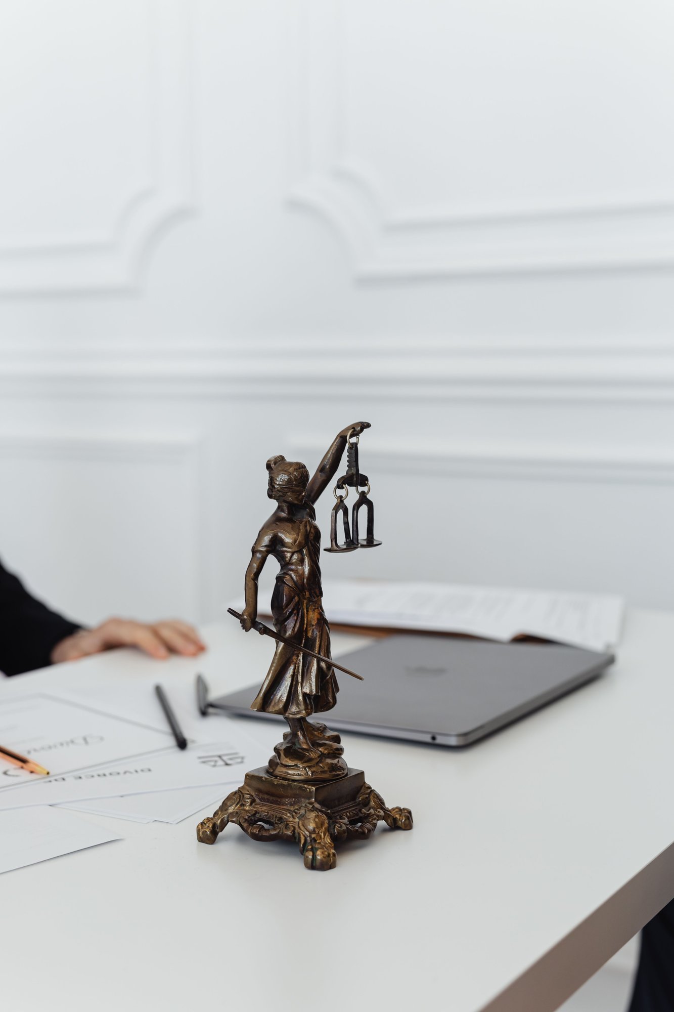 A small bronze figure of Justice on a white desk beside a closed laptop.