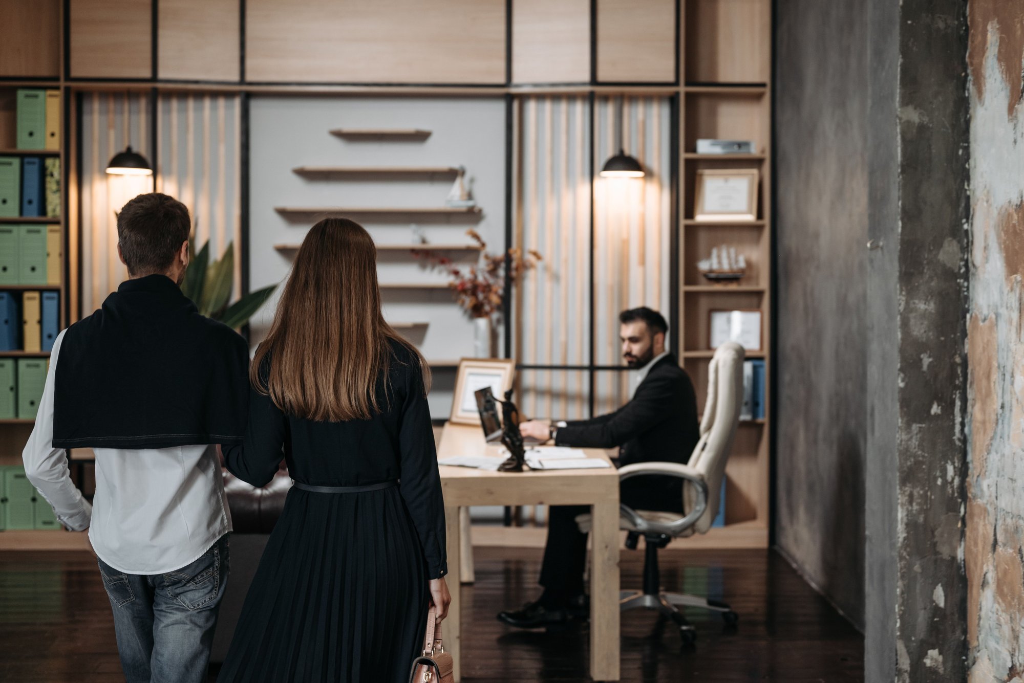 A couple walking into a modern office towards a man at a desk.