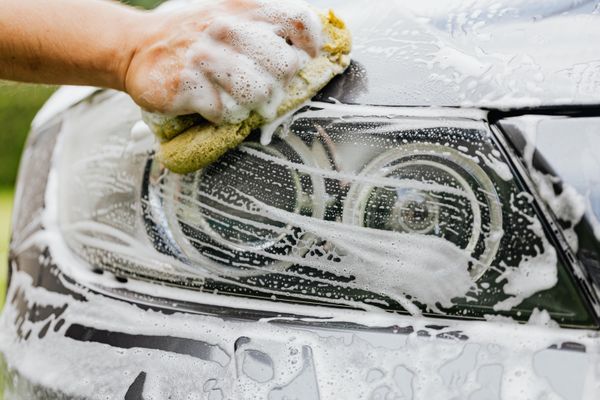 A headlight being washed by hand with a sponge and suds