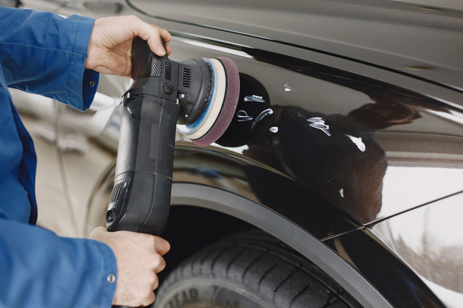 A detailer machine-polishing the black paintwork of a car