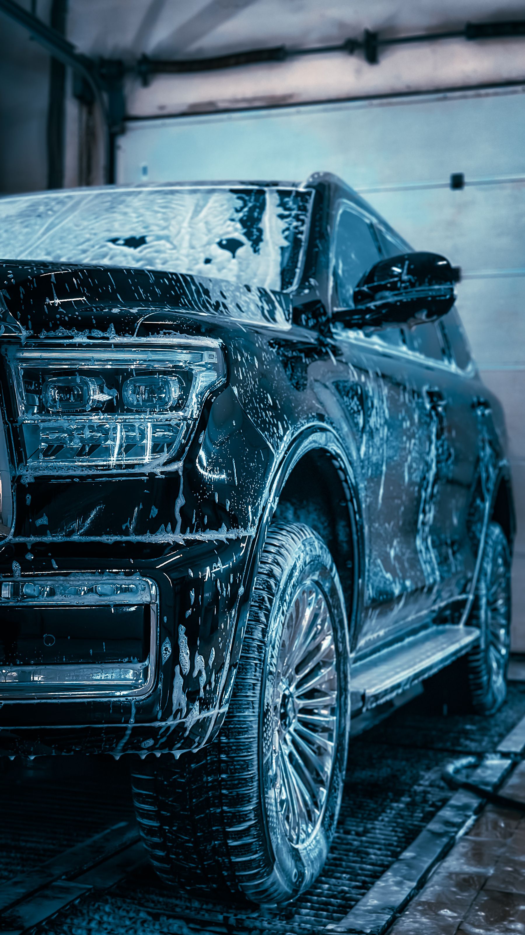 A dark SUV covered in foam during a hand wash in the shop bay