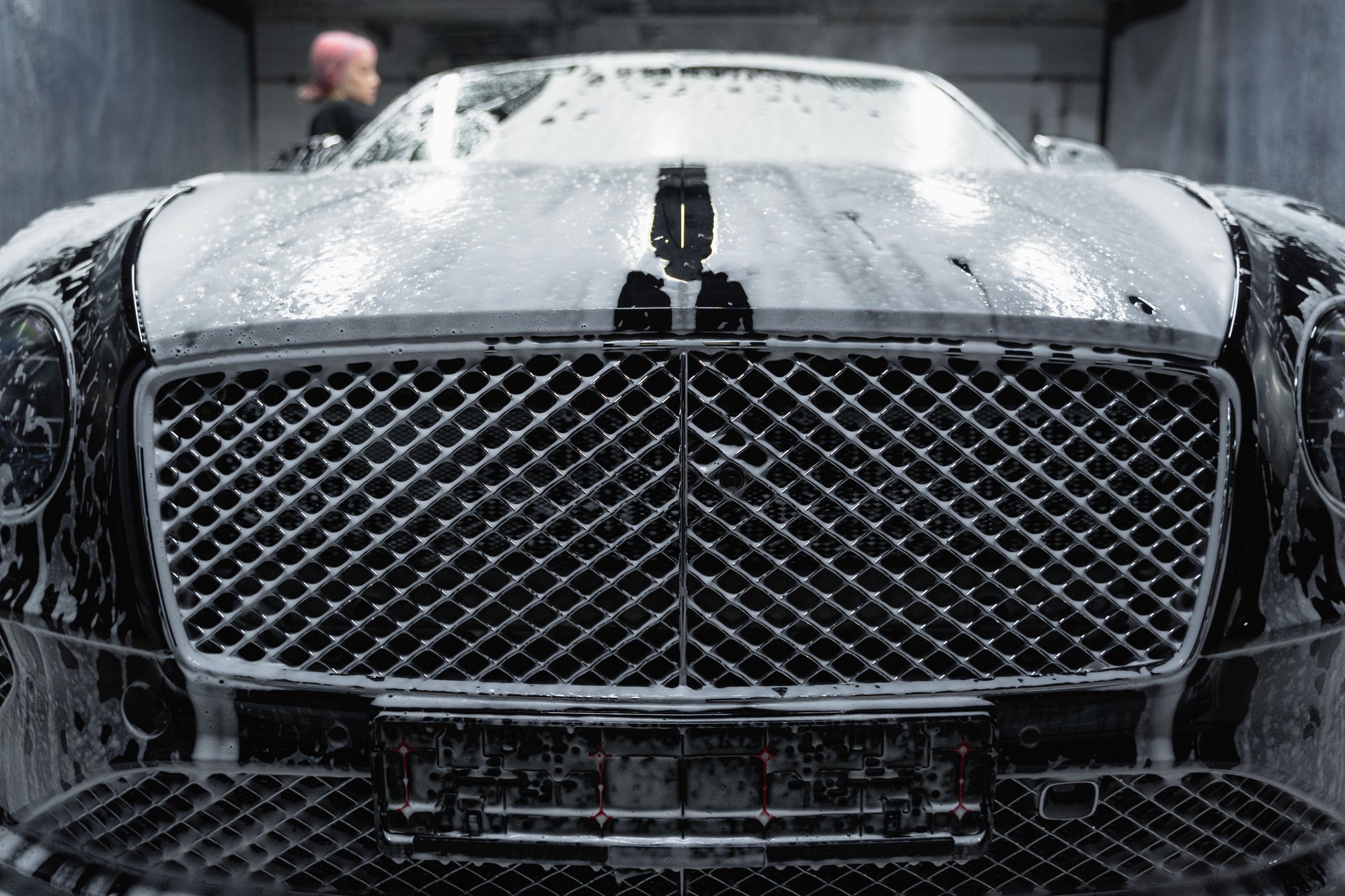 The front bumper and grille of a black car under a layer of soap suds in the wash bay.