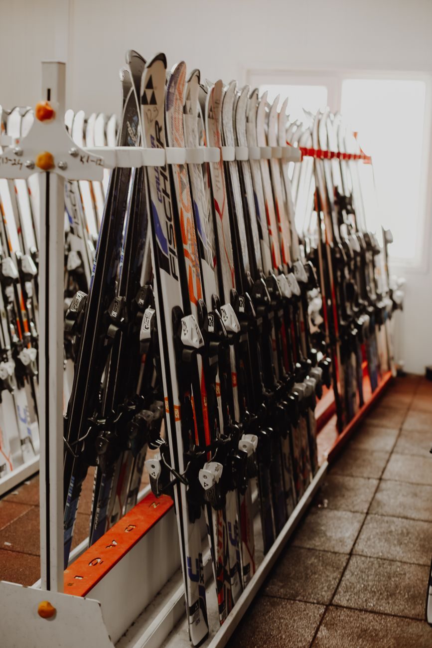 Rental skis standing on end in a long white shop rack, bindings lined up in rows, orange rack rails along the floor.