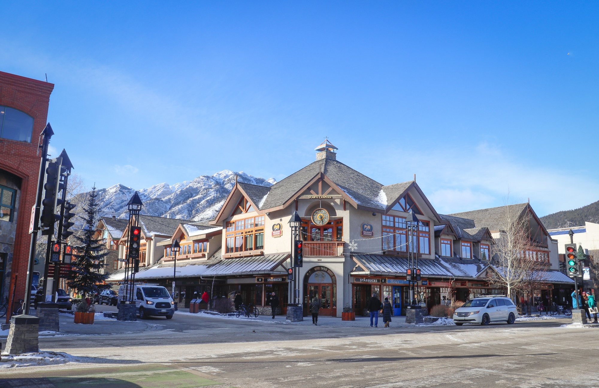 A snowy mountain-town main street with shops, a stone clock tower and peaks catching the sun behind.