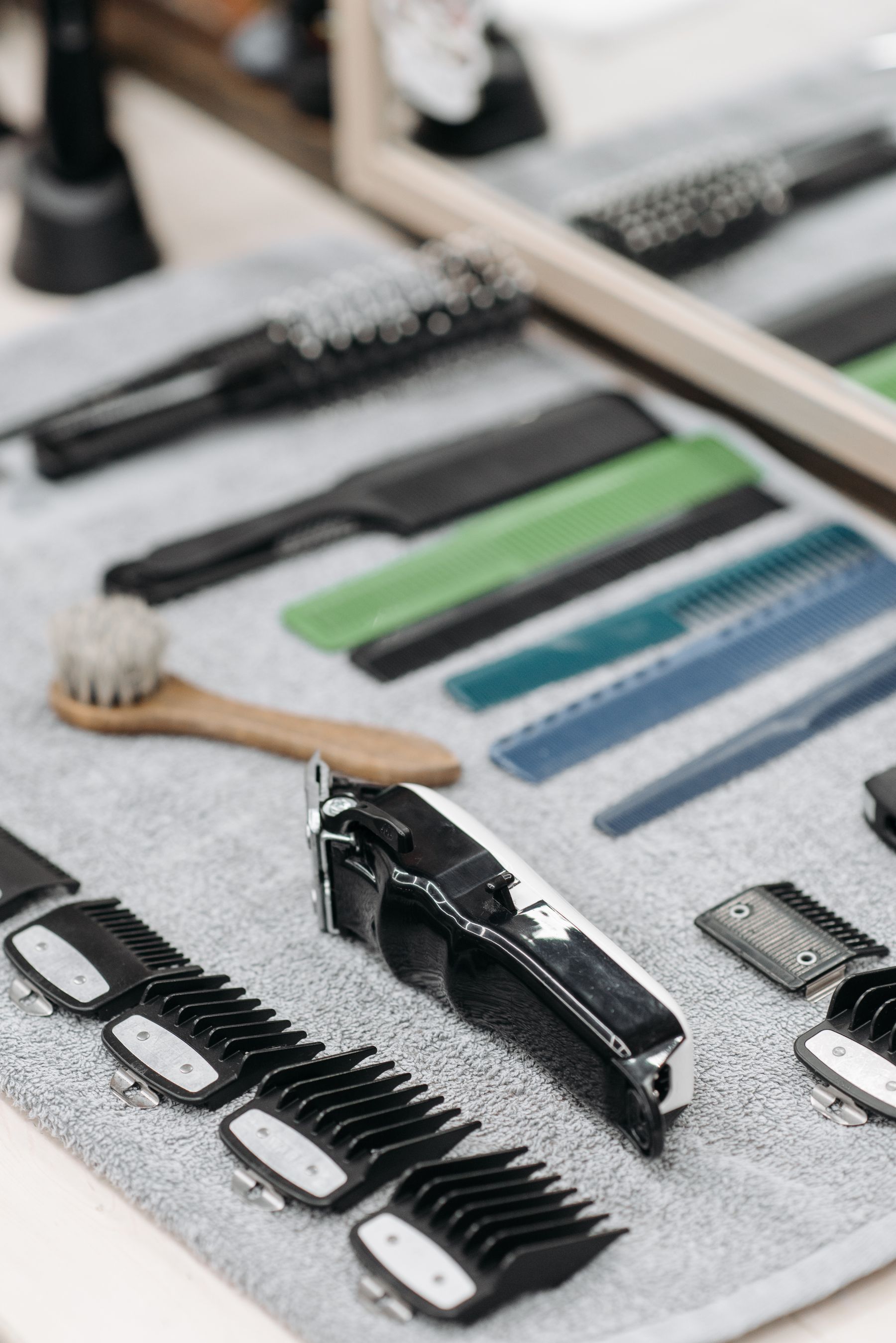 Grooming tools laid out on a grey towel: combs, scissors, a slicker brush and two clippers.
