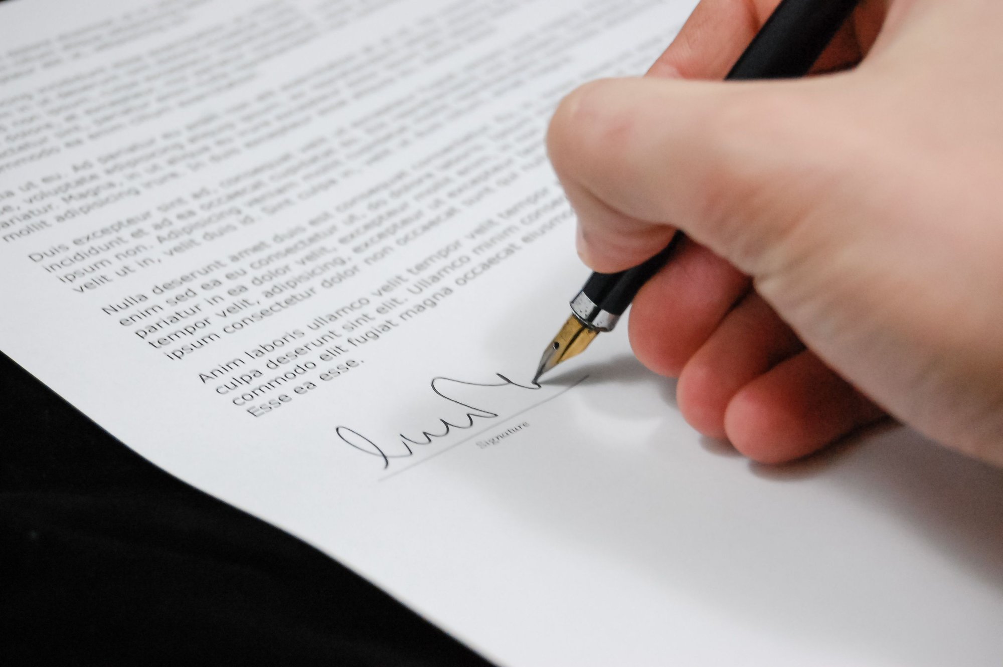 A hand signing a printed document with a fountain pen.